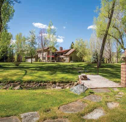 The south-facing covered front porch looks out toward the pond and wraps around the west side of the house a great place to enjoy filtered afternoon light through the aspen trees.