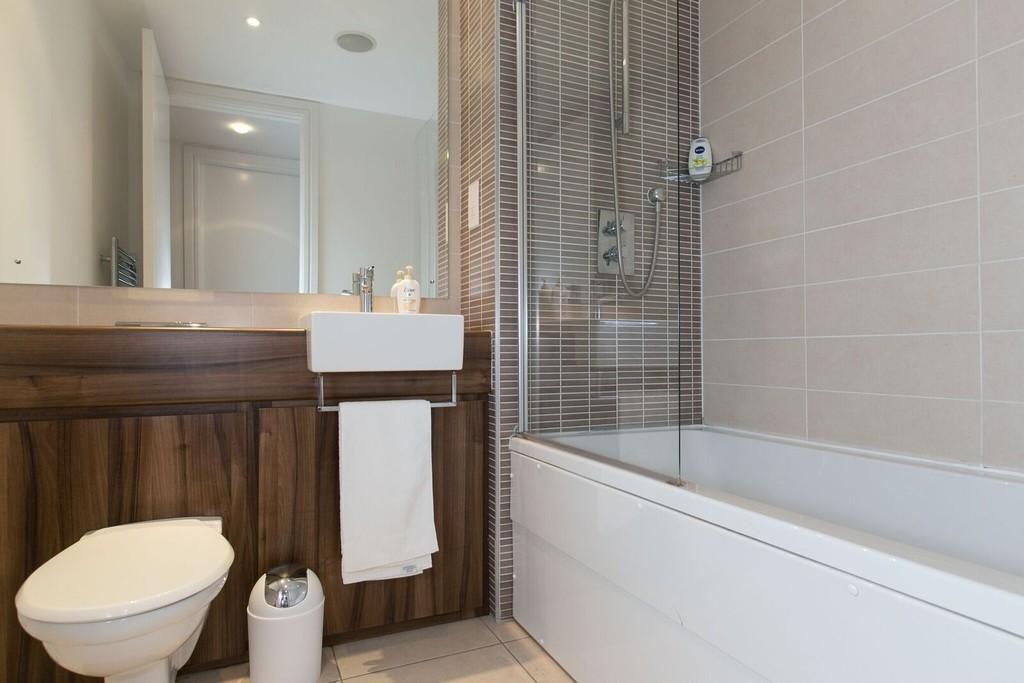 BATHROOM Modern white suite comprising WC with concealed cistern, vanity wash hand basin with integrated mirror, panelled bath with mixer taps and telephone shower attachment. Part tiled walls.