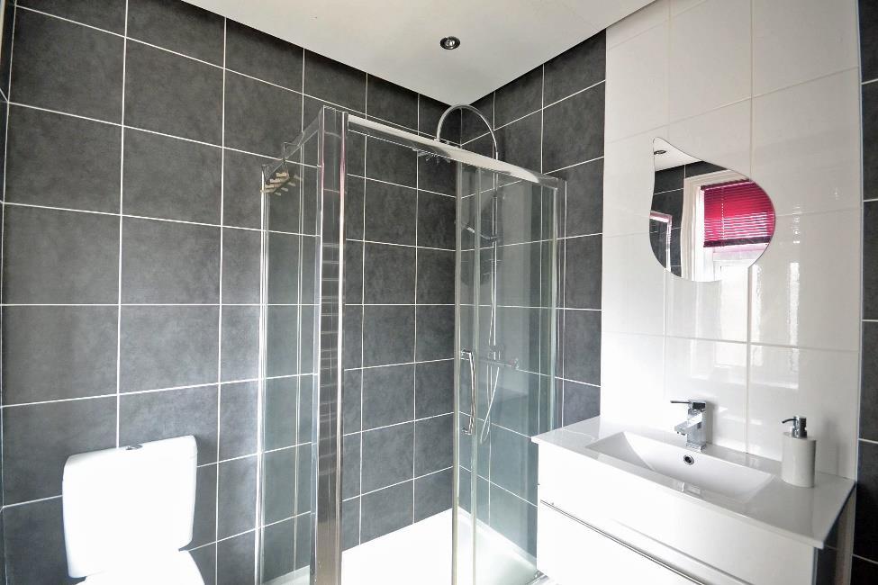 Grey tiling to the remainder of the room including around a glazed screened shower enclosure with rain head mixer shower and additional hand shower.