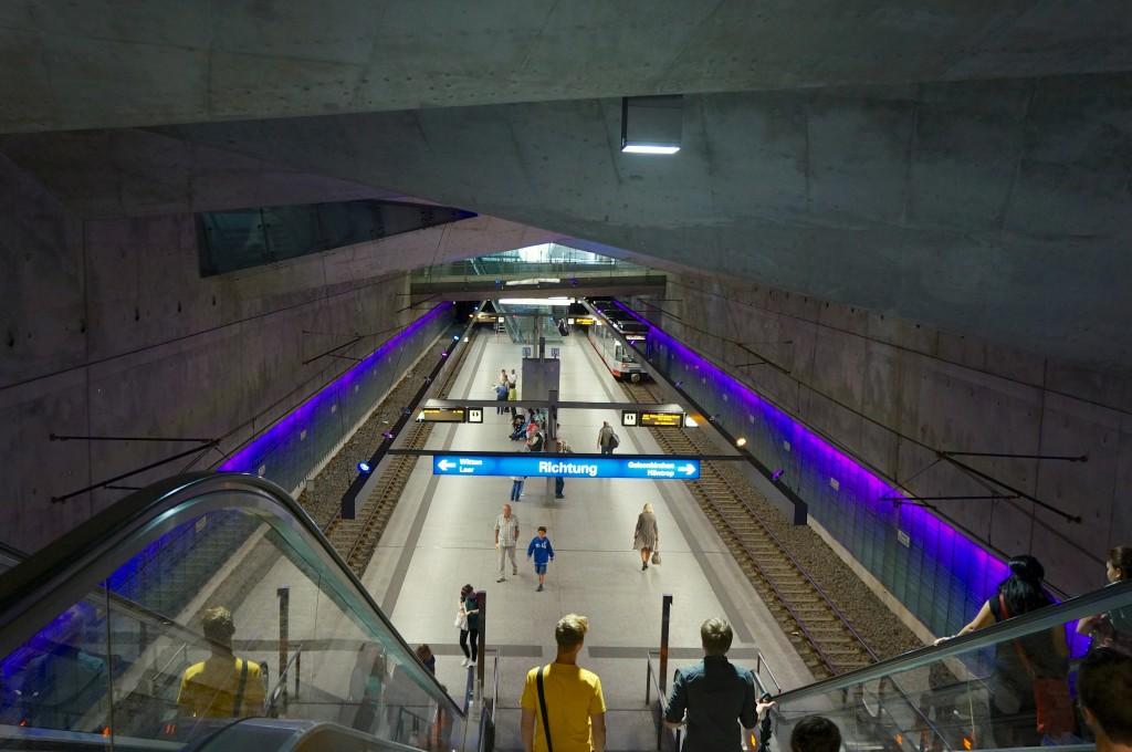while the prismatic glass bodies make the location of the station visible at the surface in urban space Two more structures penetrate the station space: A glazed sloping elevator from train to road