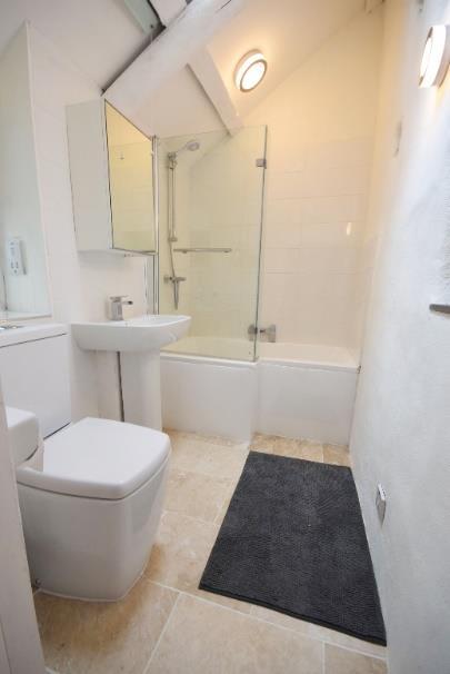 6 shower with chromium fitments, pedestal wash hand basin, low level wc, part tiled wall, travertine tiled flooring with underfloor heating, monopitch ceiling with ceiling light points and a double