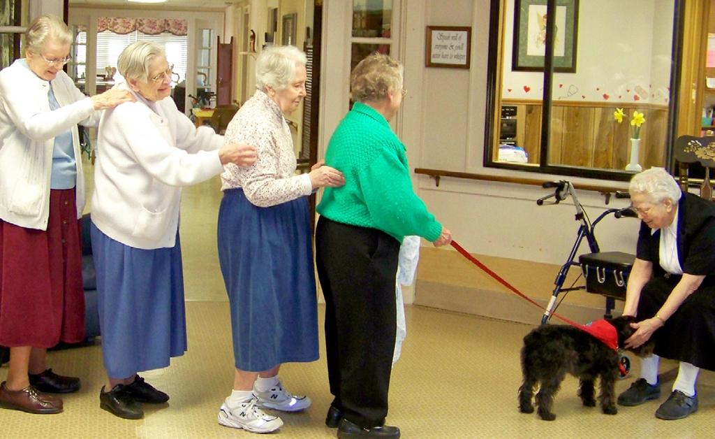 (L to R) Sisters Gabriel Brandt, Richard Walter, and Columba Moseley and visitor Iris Hightower bring Rowdy, a therapy dog, to see Sister Herbert Huber in the Infirmary.
