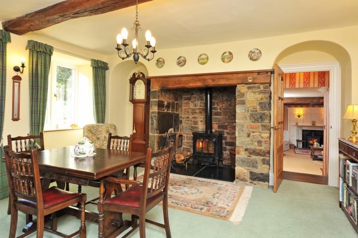 Inglenook stone fireplace with heavy wooden lintel housing woodburning stove on slate hearth.