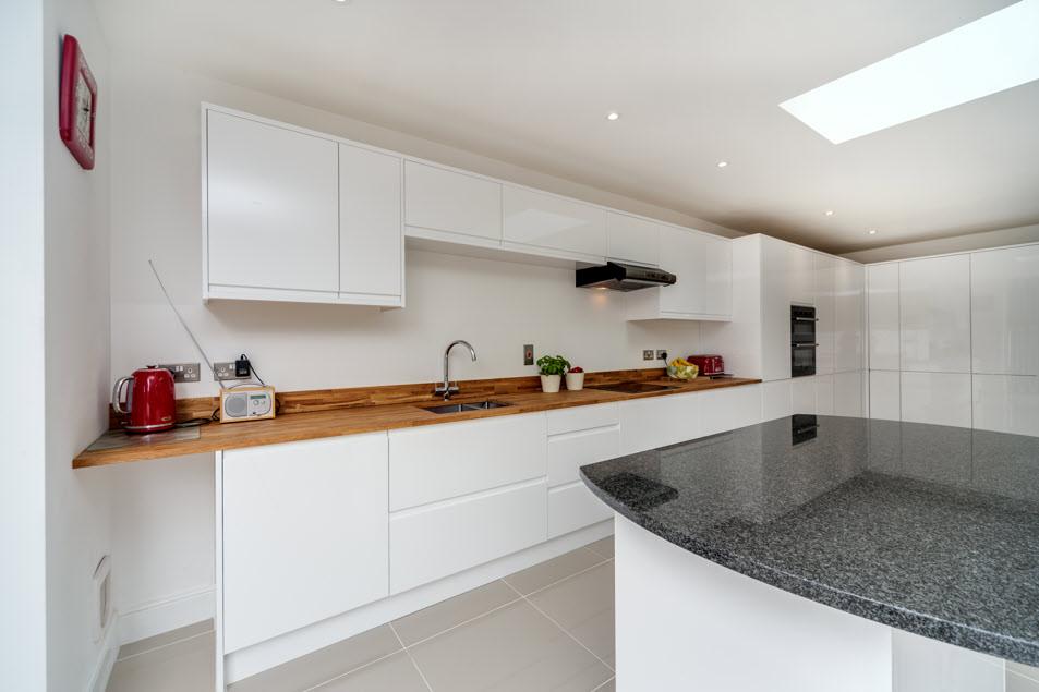Inside, the white gloss units run full-height along one wall providing a wealth of kitchen storage solutions, and within them the full height fridge, freezer, dishwasher and dual ovens have been