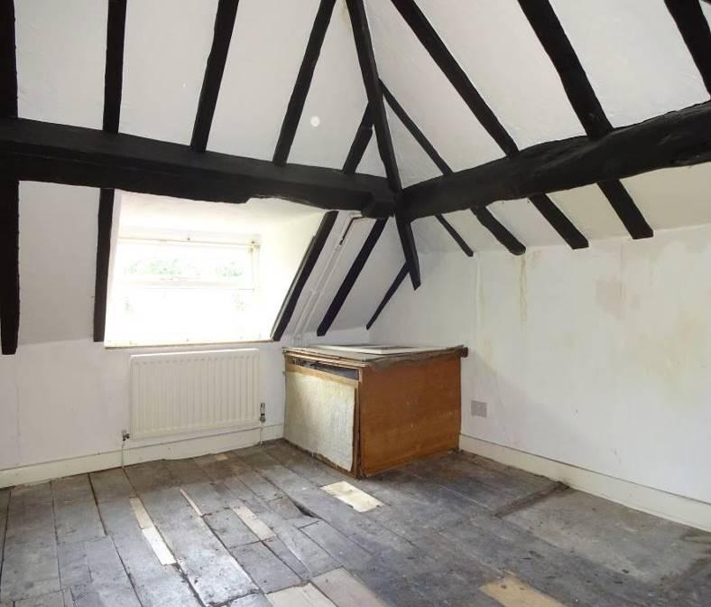 To right, a door leads into a Double Bedroom with roof eaves and exposed ceiling timbers, having featured stone walls and original wooden flooring, there is a cold water tank and a radiator.