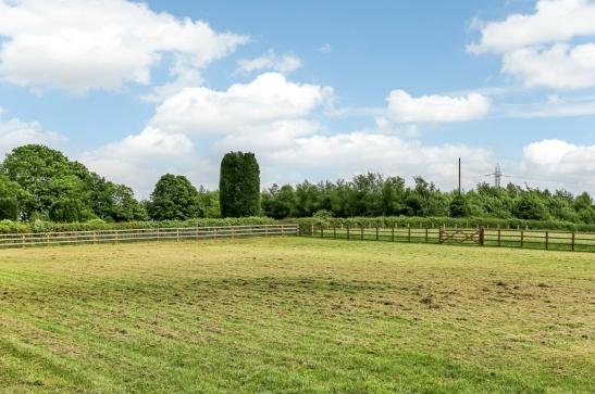 The flagstone terrace is bordered by a well kept lawn with timber edging and post and rail fencing adjoining the field and hedging to the side.