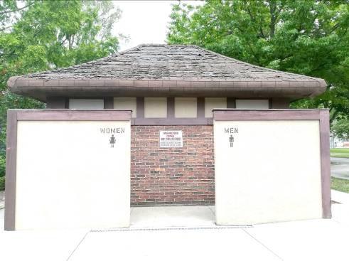 A wall with break in center surrounds the front of the washroom building with entry into the womens on the left and men s on the right.