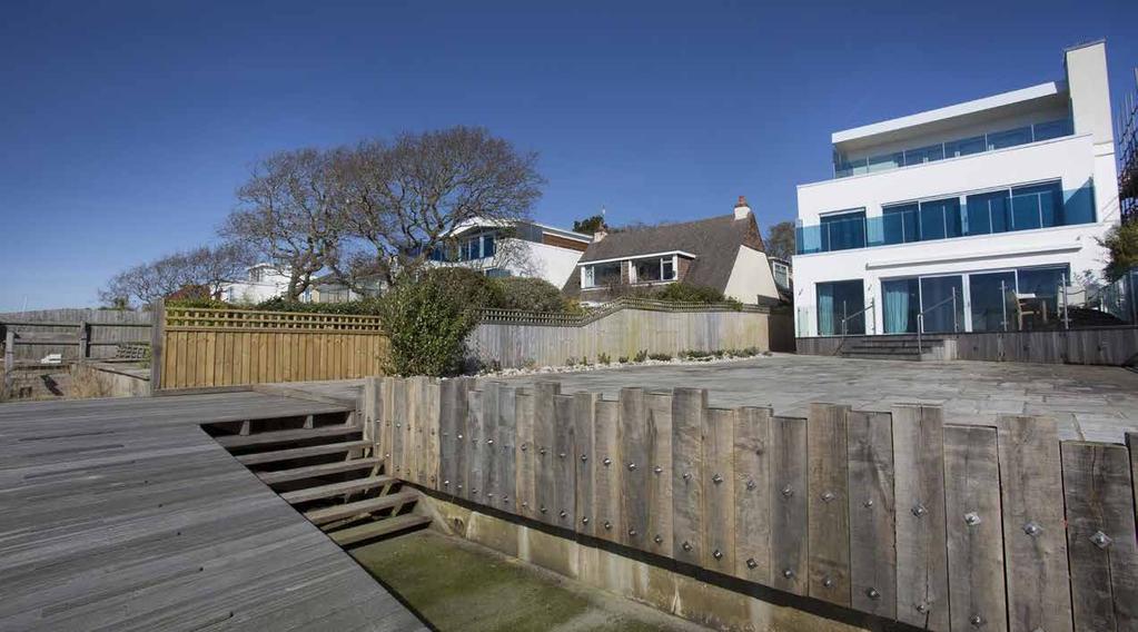 The terrace has glass balustrades and steps down to a good sized paved area with feature planted stone borders.
