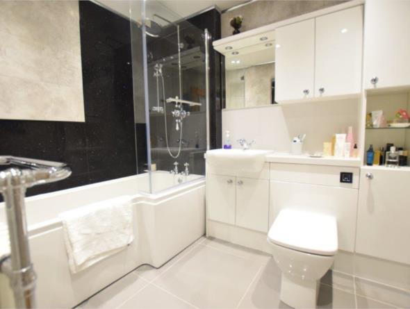 three piece suite which comprises of a L shaped shower bath, a Rak ceramic wash hand basin set into a vanity unit with inset spotlighting and high gloss height cupboards It also features a Rak low