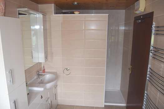Large walk-in shower lined in wetwall and tiles. Fitted mirror and medicine cabinet unit with lighting above. Ladder style towel radiator.