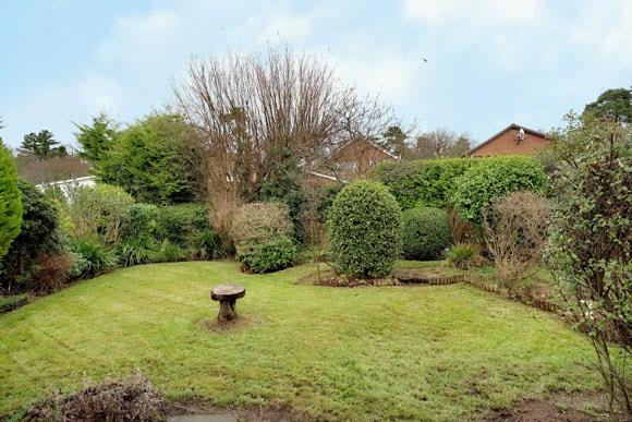 Front garden in lawn bordered by mature shrubbery.