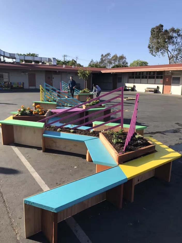The vibrant sets of benches sit at the center of a school courtyard that is devoid of color,