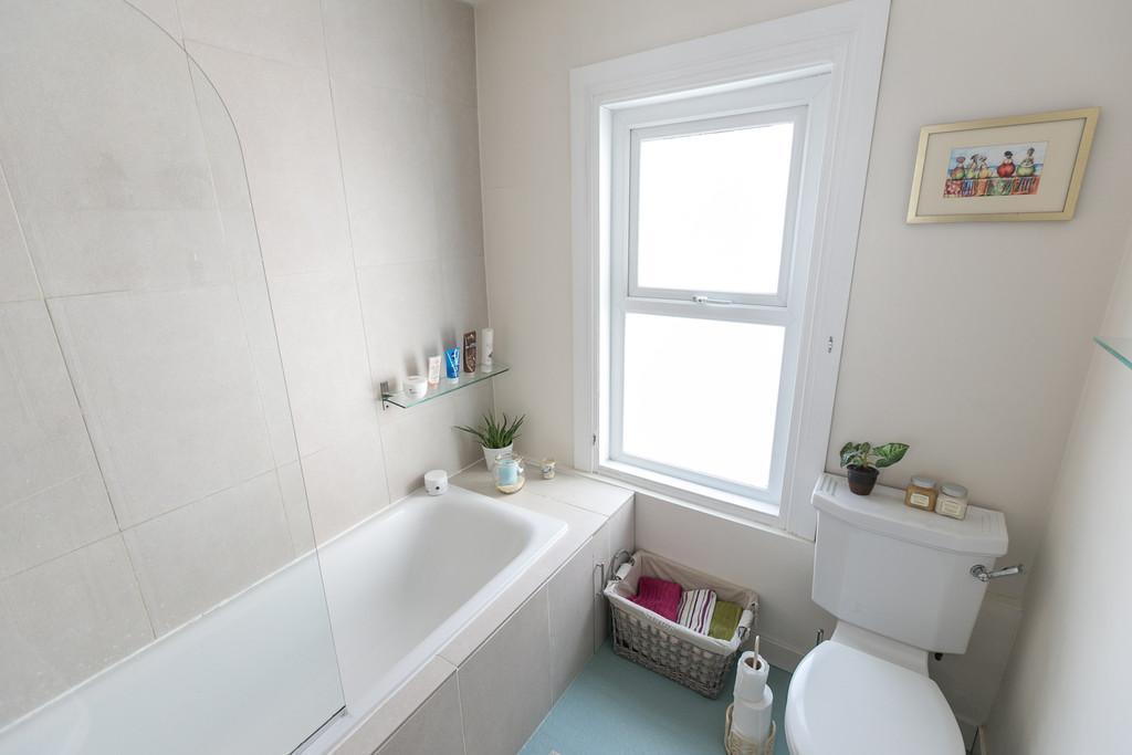 BATHROOM Modern white suite comprising bath with hand shower, pedestal wash hand basin, low flush wc, recessed low voltage spotlights, tiled walls.