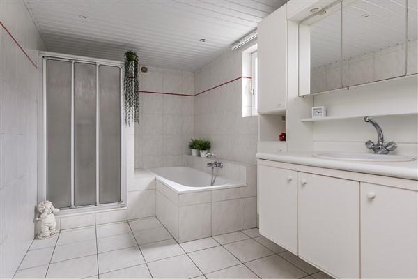 The fully tiled bathroom has a bath, a shower, a sink with cabinets and