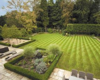 There are well manicured lawned areas with mature trees and hedging.
