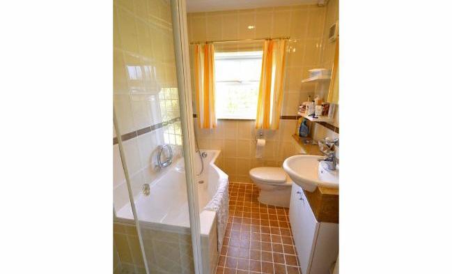 White four piece suite comprising shower cubicle, bath with shower attachment over, low level WC with concealed cistern and wash hand basin set into vanity unit with mirrored cabinet above.