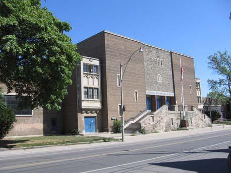 Attention is focused on the principal (west) façade facing Bathurst Street where a square tower displays multi-sided buttresses, balustrades, decorative stonework and narrow lancet windows.