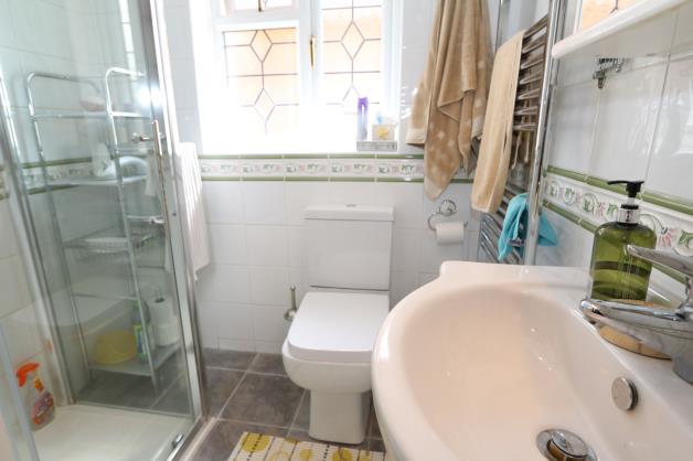 with white high gloss unit below, ceramic floor tiles, fully tiled walls, chrome heated ladder style towel radiator, extractor fan, upvc obscure double glazed lead light window to side.