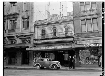 Image: Alexander Turnbull Library ref: 114/521/01-G 1950 Two men, a Vauxhall car and a number of shops and businesses in