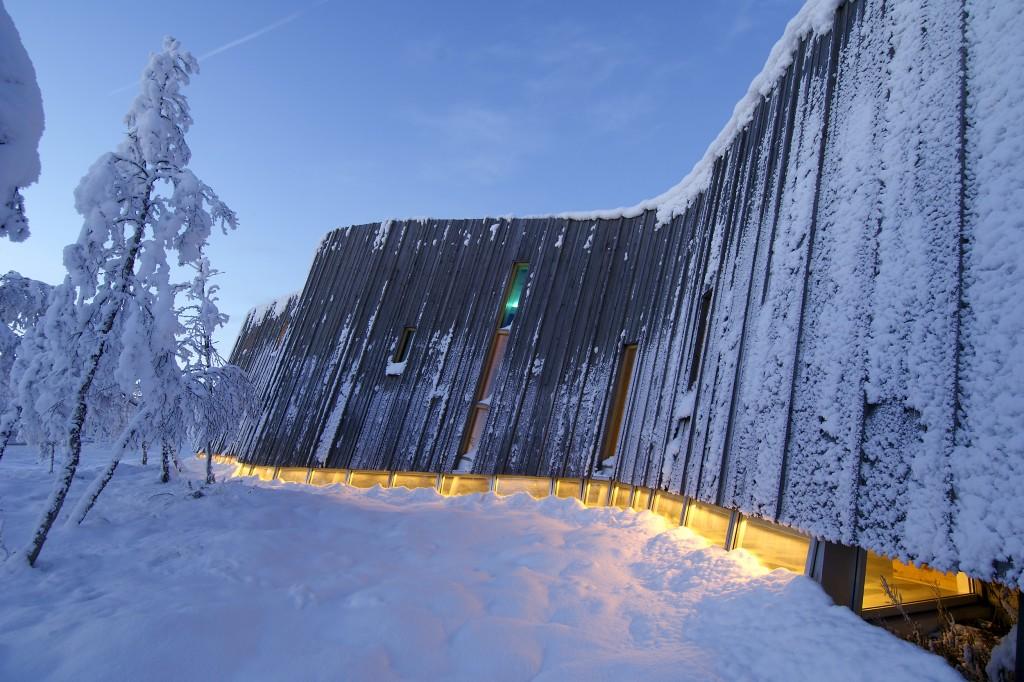 vertical larch The slanting walls of the exterior make the snow stay on the façades and the building this way transforms into an element of nature Small coloured glass tints the interiors and the