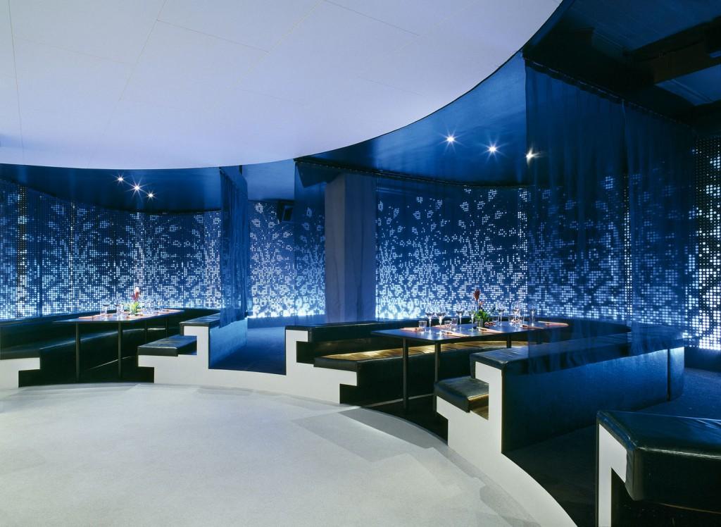 integrated into a slightly elevated podium shaped around the bar As the night advances the volume of the music rises and soft lighting changes into pulsing bright colours The lighting walls are made