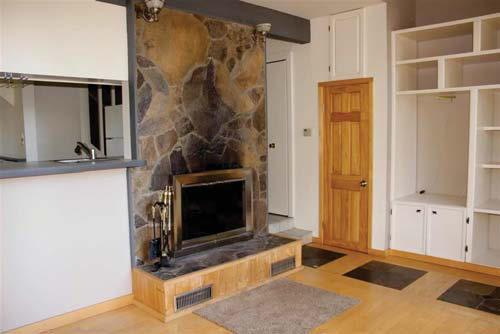 Living room has a wood burning fireplace, shelf unit and opens onto a sunny deck with