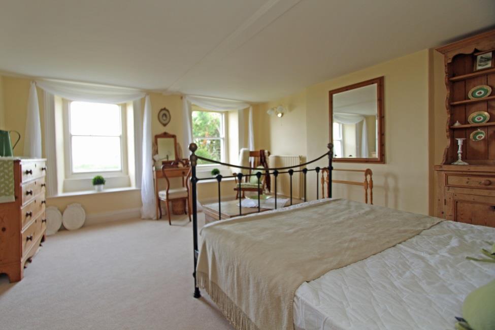 Bedroom 2 15 x 13 7 Large double bedroom with under stairs storage cupboard and 2 sash windows to front with window seats and views over agricultural fields and sea beyond.