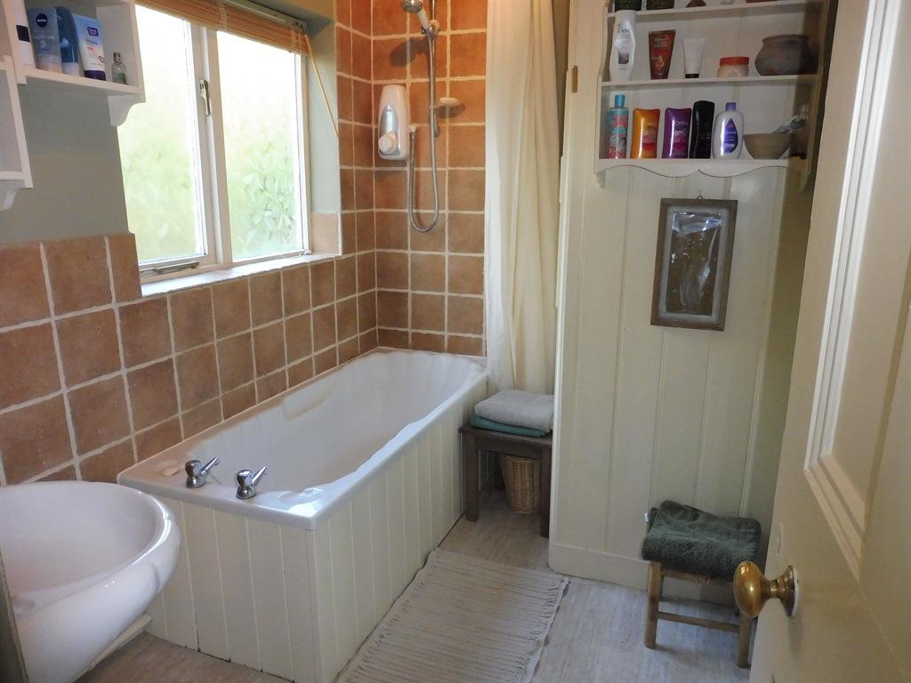 First Floor Bathroom briefly comprising a panelled bath with an electric shower over, wash hand basin, single glazed window to the rear, part tiling to walls, tiled flooring and having built in